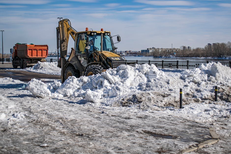 Excavator and truck working on snow removal in a winter town setting.